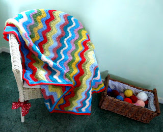 colorful ripple crochet blanket on wicker chair next to a basket of yarn