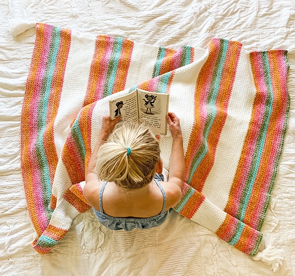 woman reading a book with a linen stitch crochet blanket on her lap