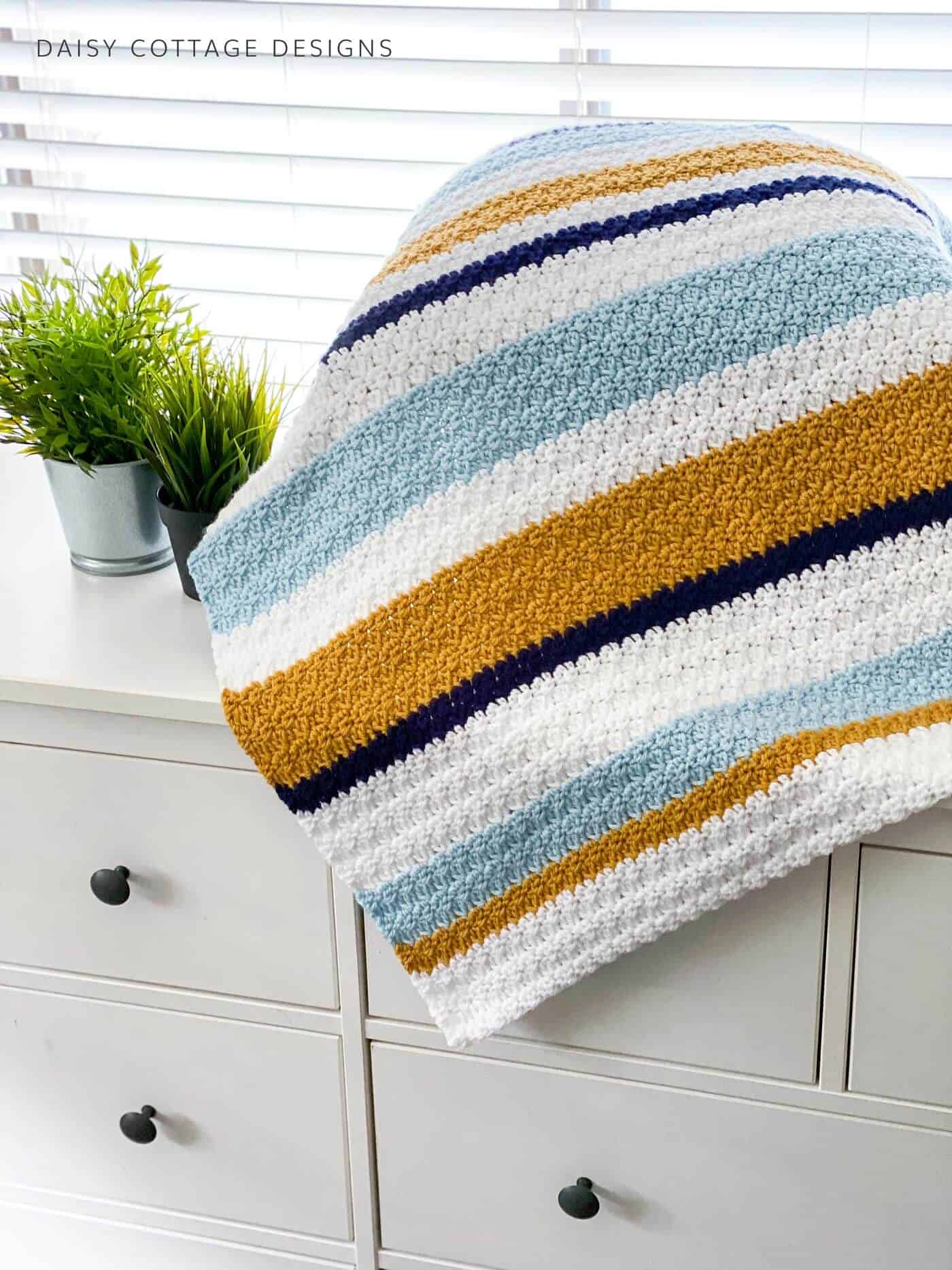 striped crochet blanket on a cabinet next to window blinds