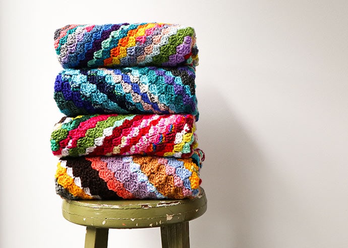 folded c2c crochet blankets stacked on top of each other on a wooden stool
